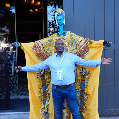 一名男子在世界旅游市场（World Travel Market）与一座传统非洲雕塑合影
