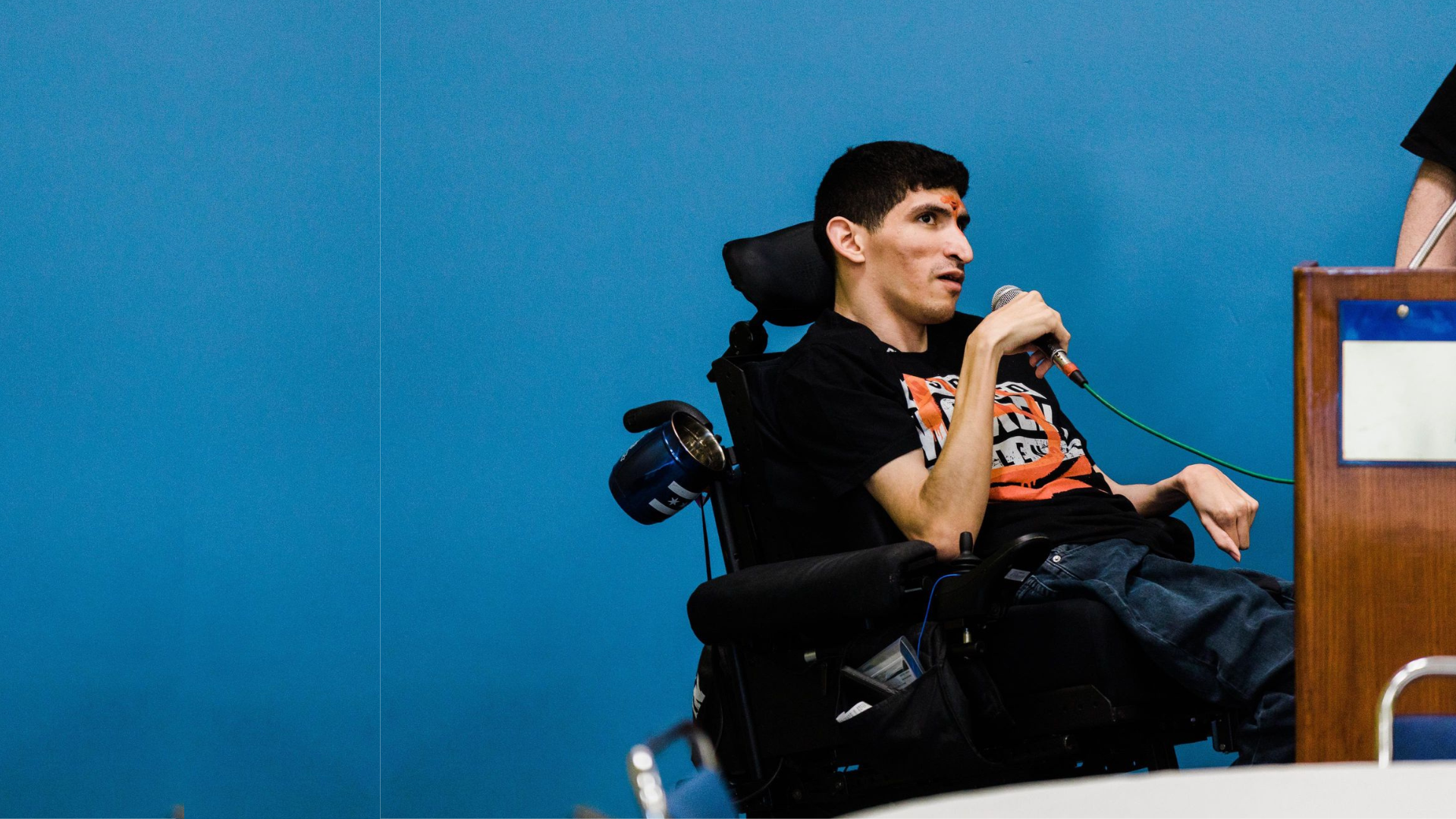 Man sat in a wheelchair speaking to an audience holding a microphone